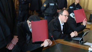 Angeklagte im Bremer Gericht mit Akten vorm Gesicht. Dazwischen ein Verteidiger