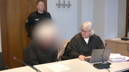 Der Angeklagte berät sich mit seiner Anwältin im Gerichtssaal, sein Gesicht ist unkenntlich gemacht
