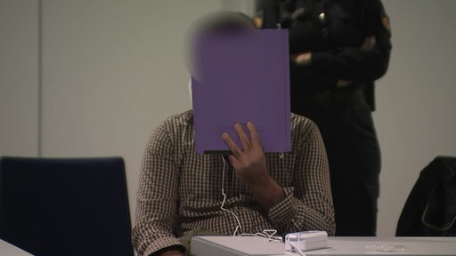 Der Angeklagte verdeckt sein Gesicht im Gerichtssaal. 