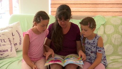 Flutopfer Angelika Hommes und ihre Kinder sitzen auf einem Sofa und lesen eine Zeitschrift.