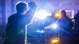 Ein Angreifer mit einem Messer bedroht Polizisten vor einem Polizeiauto. (Symbolbild)