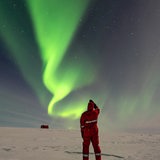 Ein Mann beobachtet Polarlichter über einer Schneelandschaft in der Antarktis.