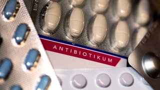 Eine Packung Antibiotika (M) und diverse andere Medikamente liegen auf einem Tisch in einer Apotheke. 