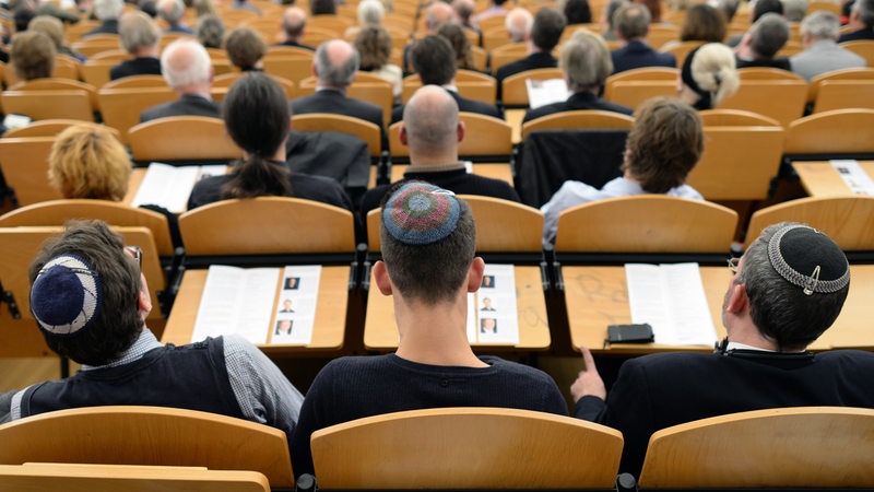 In einem vollbesetzten Hörsaal sitzen sieht man 3 Studierende mit einer Kippa auf dem Kopf.