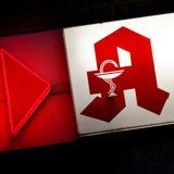 Ein Leuchtschild weist mit roten Pfeilen auf das Apotheken-Logo.