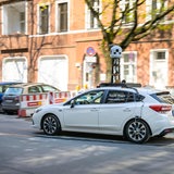 Ein Auto mit einem Stativ auf dem Dach fährt durch eine Stadt