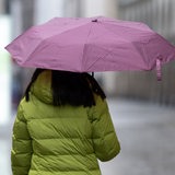 Eine Frau von hinten mit Regenschirm und Winterjacke (Symbolbild)