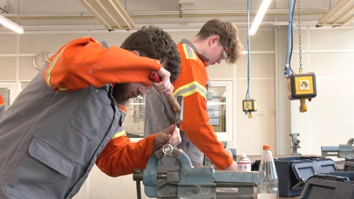 Zwei Auszubildende in Schutzklamotten bei der Arbeit.