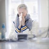  Eine Frau sitzt an einem Tisch und putzt sich die Nase (Symbolfoto)