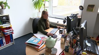 Es sitzt eine Frau in einem Büro an dem Schreibtisch.