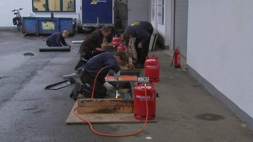 Es sind mehrere Dachdecker bei der Arbeiten zu sehen.