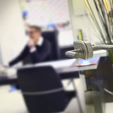 Blick durch eine offene Glastür in einem Büro. Ein Mann sitzt an seinem Schreibtisch (Symbolbild)