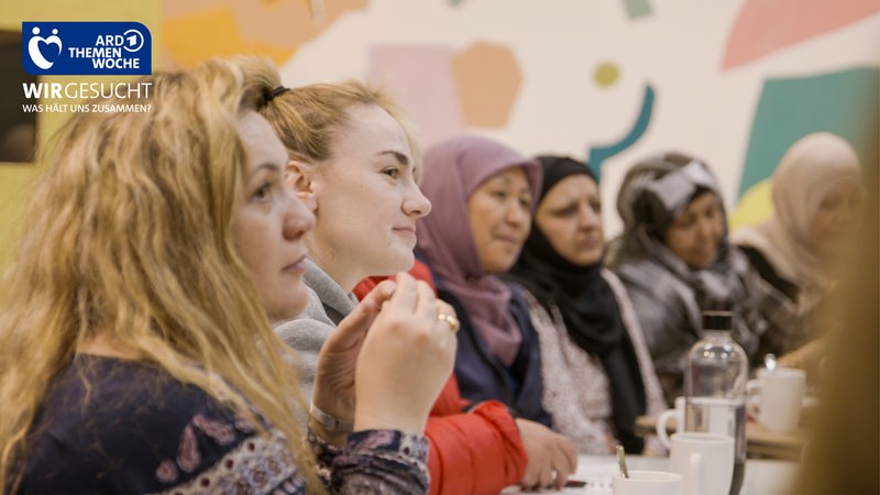 Frauen sitzen an einem Tisch und lächeln, sie sind Teil des Café Global bei dem sie Deutsch lernen.