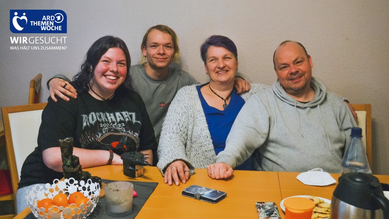 Vier Menschen, Familie Lorenz, sitzt an ihrem Esstisch und schaut in die Kamera.