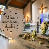 Ein Luftballon mit der Aufschrift "Wir vermissen dich!" schwebt bei der Trauerfeier für Arian aus Bremervörde vor einem mit Blumen geschmückten Altar.