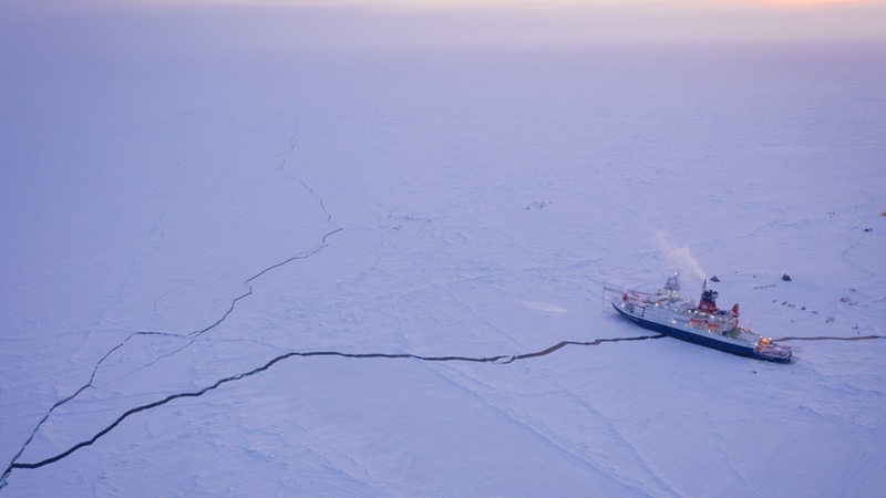 Ein Eisbrecher liegt umgeben von einer großen Eisfläche in der Arktis.