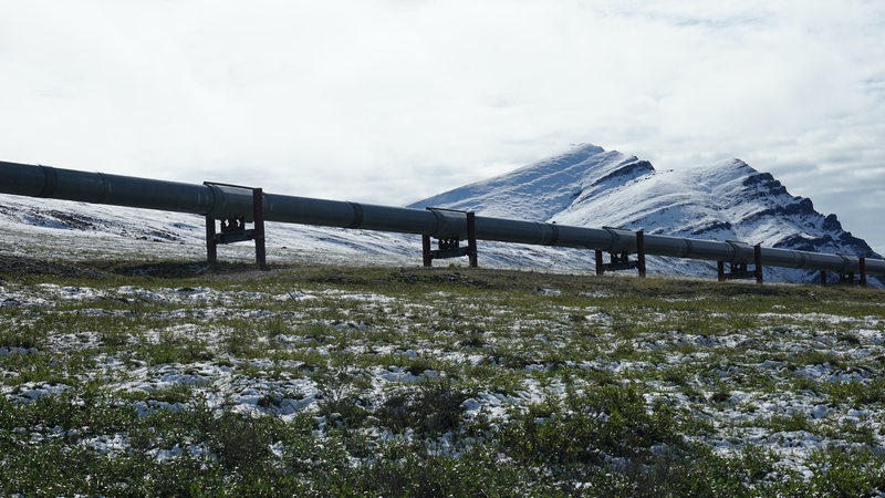 Eine Pipeline führt über eine verschneite Wiese vor einem Berg entlang.