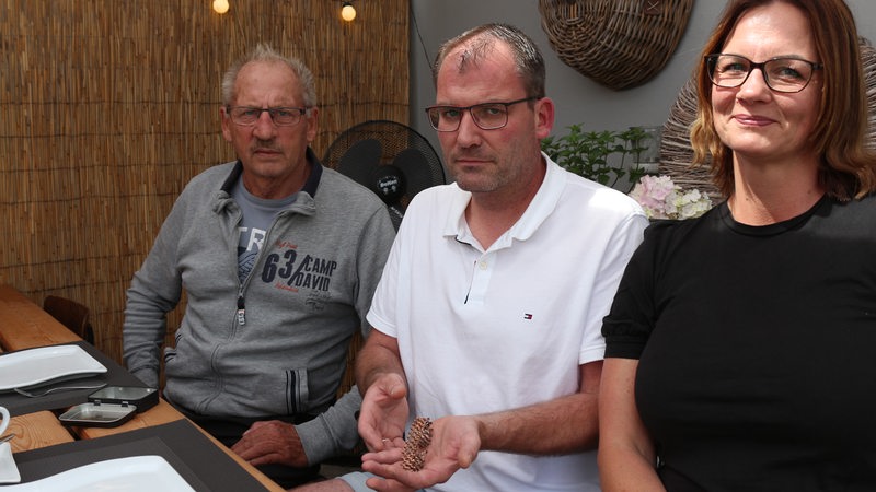 Thomas Franz hält das Armband vorsichtig in seiner Hand, Joachim Franz und Yvonne Franz sitzen neben ihm