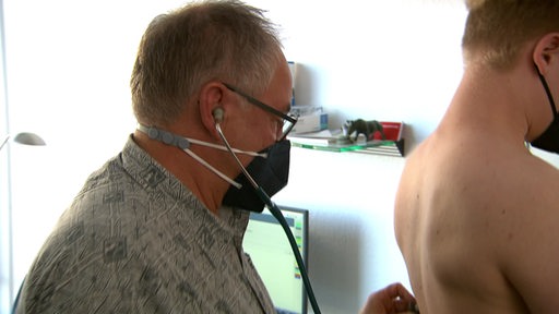 Zu sehen ist ein Arzt der einen Patienten mit einem Stethoskop abhört.