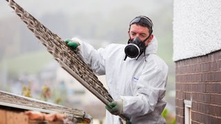 Ein Mann in Schutzkleidung trägt Asbest-Material aus einem Wohnhaus (Archivbild)