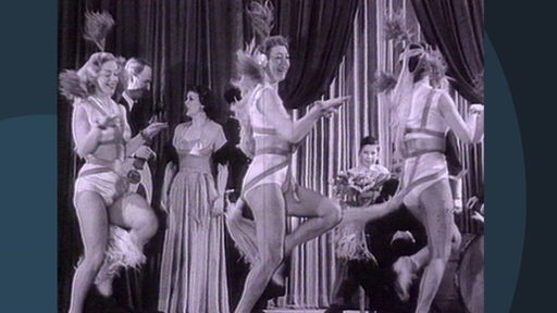 Eine Archivaufnahme von drei Variete Tänzerinnen während einer Show auf einer Bühne.