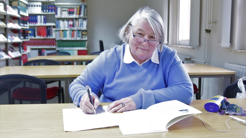 Eine Frau sitzt an einem Tisch und schreibt in ein Heft.