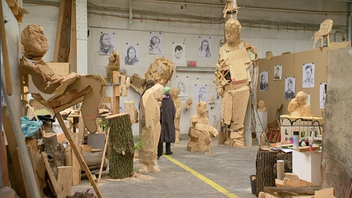Große Holzskulpturen von Menschen stehen in einem Atelier