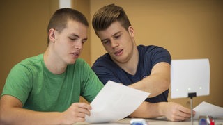 Zwei junge Männer lesen ein Papier.