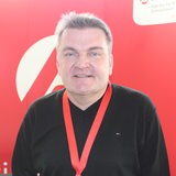 Ein Mann mit Schlüsselband um den Hals steht vor einer roten Wand.