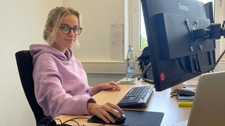 Junge Frau sitzt am Schreibtisch vor Computer.