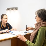 Eine Patientin wird an der Rezeption einer Arztpraxis von der Sprechstundenhilfe beraten.