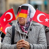 Eine Frau mit Kopftuch ist hinter einer deutschen und 2 türkischen Fähnchen zu sehen.