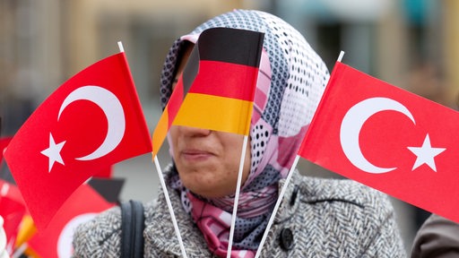 Eine Frau mit Kopftuch ist hinter einer deutschen und 2 türkischen Fähnchen zu sehen.