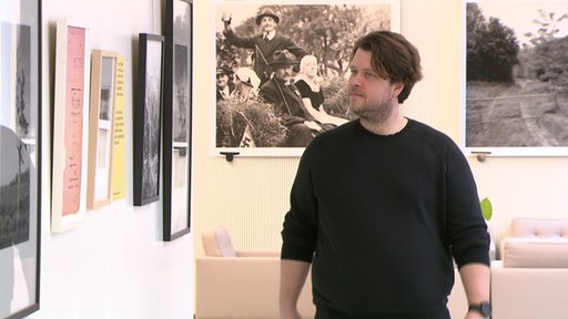 Der Fotograf Stefan Weger geht durch seine Ausstellung und schaut Bilder an. 