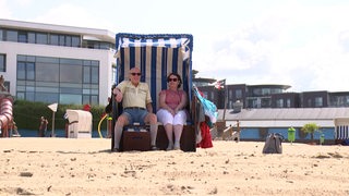 Zwei Personen sitzen in einem Strandkorb an einem Strand.