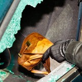 Ein Dieb stiehlt eine Handtasche durch ein eingeschlagenes Autofenster