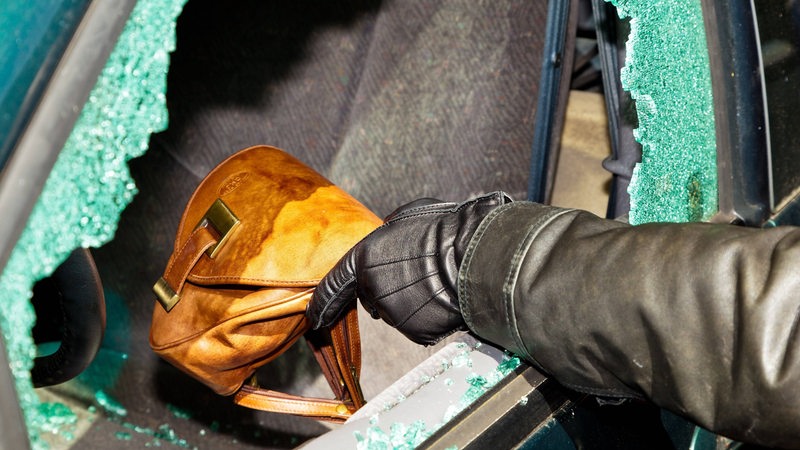 Ein Dieb stiehlt eine Handtasche durch ein eingeschlagenes Autofenster