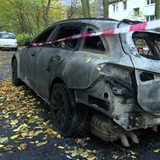 Ein ausgebranntes Auto steht am Straßenrand.