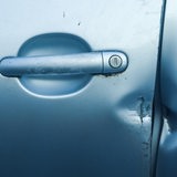 Eine Tür eines Autos mit einer Delle, die auf einen Einbruch schließen lässt.