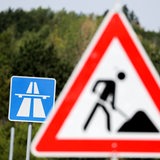 Zwei Schilder stehen hintereinander vor grünen Bäumen.