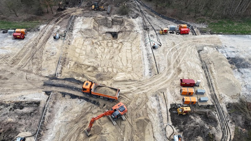 Mehrere Baustellenfahrzeuge stehen auf einer Sandfläche.