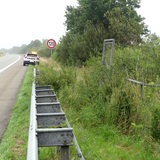 Links parkt ein Auto mit Warnlicht auf dem Dach am Rande einer Autobahn. Rechts ist ein mit Büschen bewachsener Graben zu sehen.