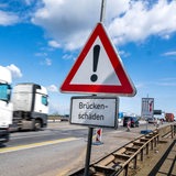 Auf der Weserbrücke der A1 in Bremen fahren Lastwagen. Im Vordergrund ist ein Warnschild mit dem Hinweis "Brückenschäden" zu sehen.