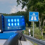 Ein Polizeiauto mit Blaulicht steht vor einem Autobahnschild.