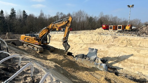 Ein Bagger ssteht in einer Sandgrube und arbeitet an einer beschädigten Röhre.