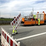 Bauarbeiter räumen eine Absperrung auf einer Straße weg.