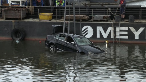 Ein schwarzer Mercedes wird mittels Kran aus dem Wasser geborgen.