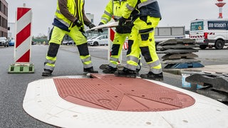 Drei Bauarbeiter arbeiten an einem Hindernis auf einer Straße.