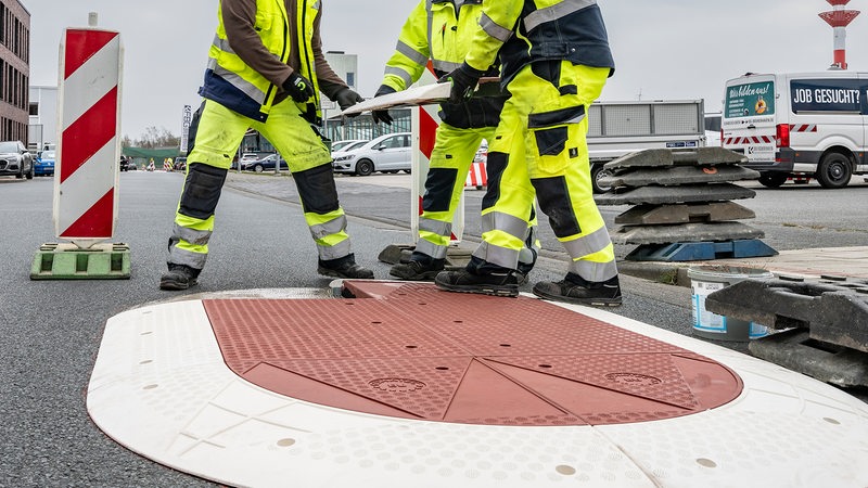Drei Bauarbeiter arbeiten an einem Hindernis auf einer Straße.