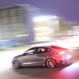 Ein sportliches Auto fährt vor verwischtem Hintergrund auf einer Straße.